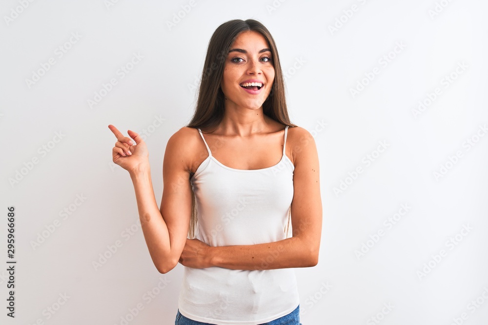 Young beautiful woman wearing casual t-shirt standing over isolated white background with a big smile on face, pointing with hand and finger to the side looking at the camera. Young beautiful woman wearing casual t-shirt standing over isolated white background with a big smile on face, pointing with hand and finger to the side looking at the camera.