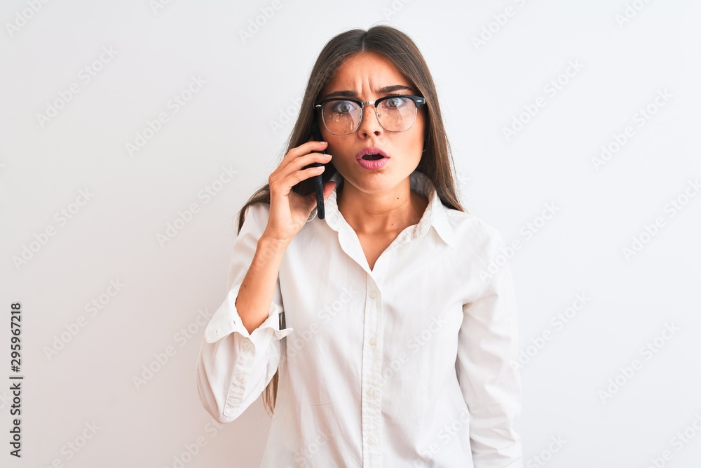 Young businesswoman wearing glasses talking on smartphone over isolated white background scared in shock with a surprise face, afraid and excited with fear expression Young businesswoman wearing glasses talking on smartphone over isolated white background scared in shock with a surprise face, afraid and excited with fear expression