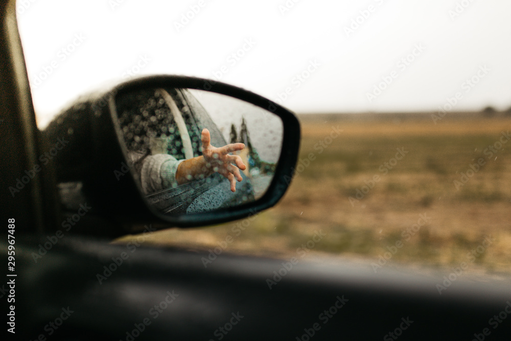 Hand touching rain drops. Mirror seen through the glass. Wet car window. Close up rain drop. Car view see the mirror. Rainy day. Hand touching rain drops. Mirror seen through the glass. Wet car window. Close up rain drop. Car view see the mirror. Rainy day.
