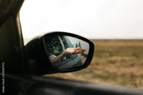 Hand touching rain drops. Mirror seen through the glass. Wet car window. Close up rain drop. Car view see the mirror. Rainy day. © EGHStock