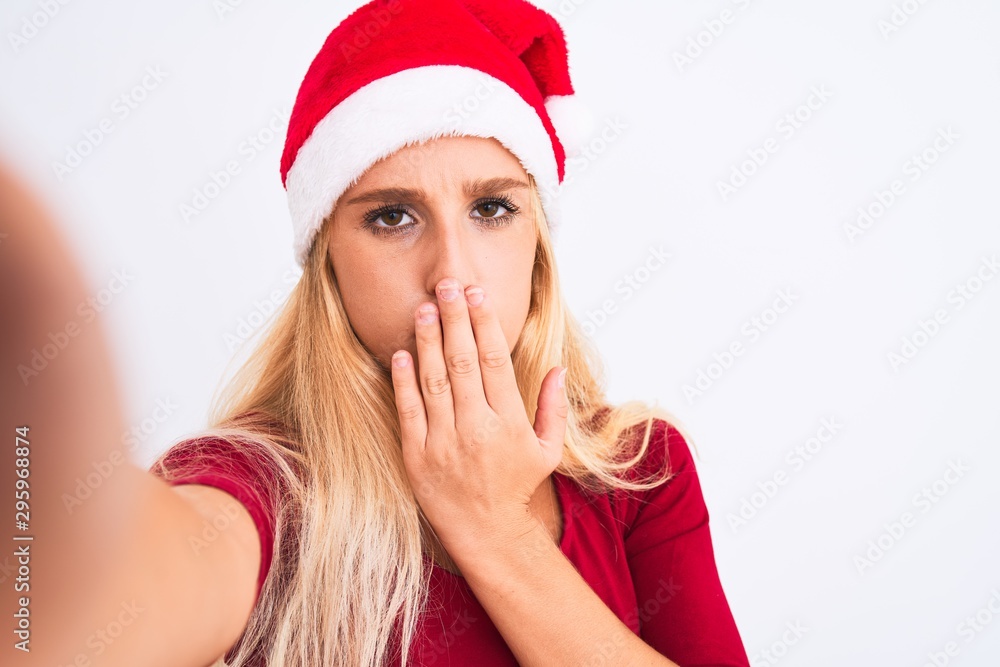 Woman wearing Christmas Santa hat make selfie by camera over isolated white background cover mouth with hand shocked with shame for mistake, expression of fear, scared in silence, secret concept Woman wearing Christmas Santa hat make selfie by camera over isolated white background cover mouth with hand shocked with shame for mistake, expression of fear, scared in silence, secret concept