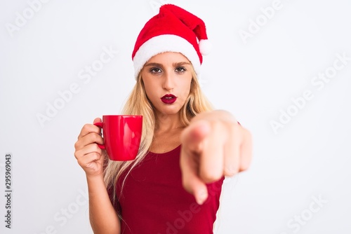 Beautiful woman wearing Christmas Santa hat drinking coffee over isolated white background pointing with finger to the camera and to you  hand sign  positive and confident gesture from the front