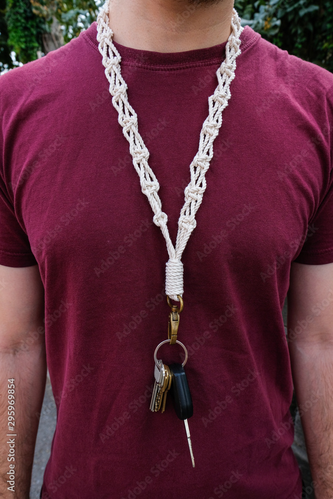 A man is wearing a long macrame keychain / lanyard around his neck that is  hanging down the front of his body. Stock Photo | Adobe Stock