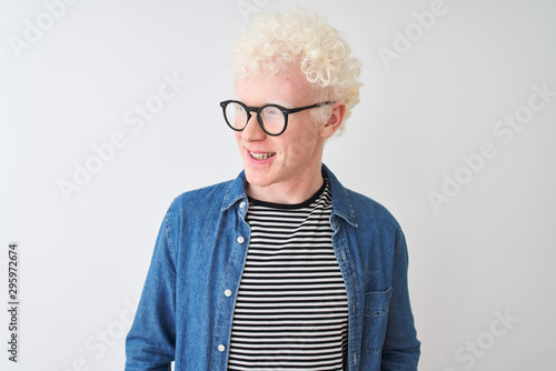 Young albino blond man wearing denim shirt and glasses over isolated white background looking away to side with smile on face, natural expression. Laughing confident.