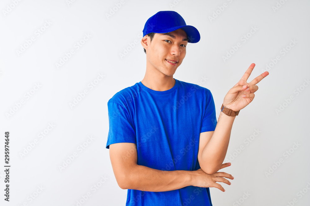 Chinese deliveryman wearing blue t-shirt and cap standing over isolated white background smiling with happy face winking at the camera doing victory sign. Number two. Chinese deliveryman wearing blue t-shirt and cap standing over isolated white background smiling with happy face winking at the camera doing victory sign. Number two.