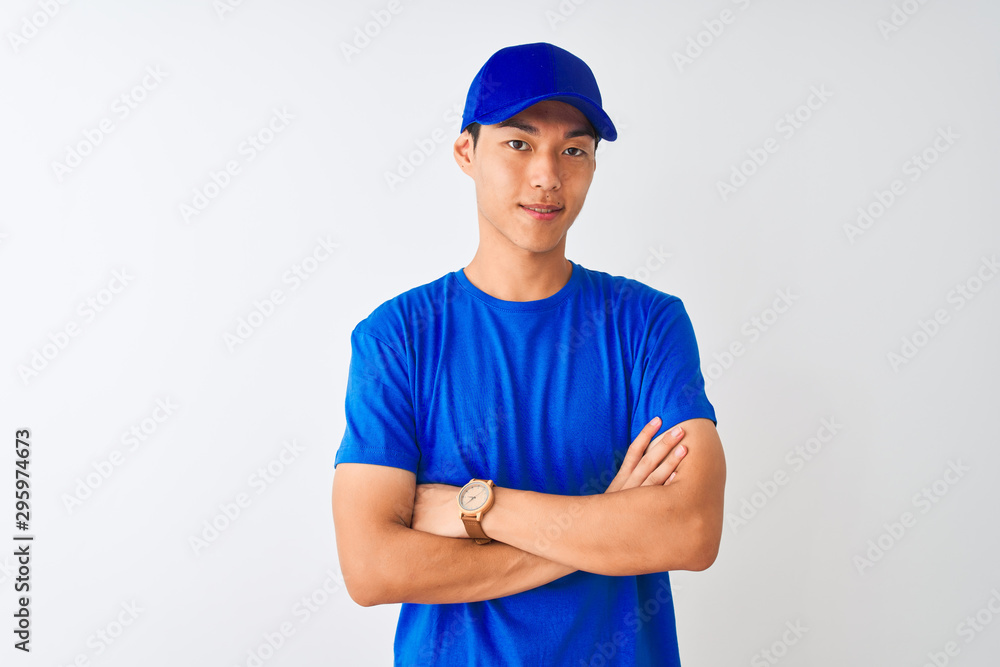 Chinese deliveryman wearing blue t-shirt and cap standing over isolated white background happy face smiling with crossed arms looking at the camera. Positive person.