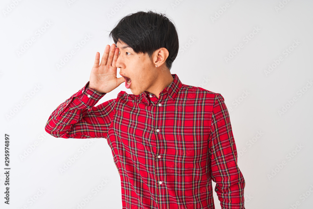 Young chinese man wearing casual red shirt standing over isolated white background shouting and screaming loud to side with hand on mouth. Communication concept. Young chinese man wearing casual red shirt standing over isolated white background shouting and screaming loud to side with hand on mouth. Communication concept.