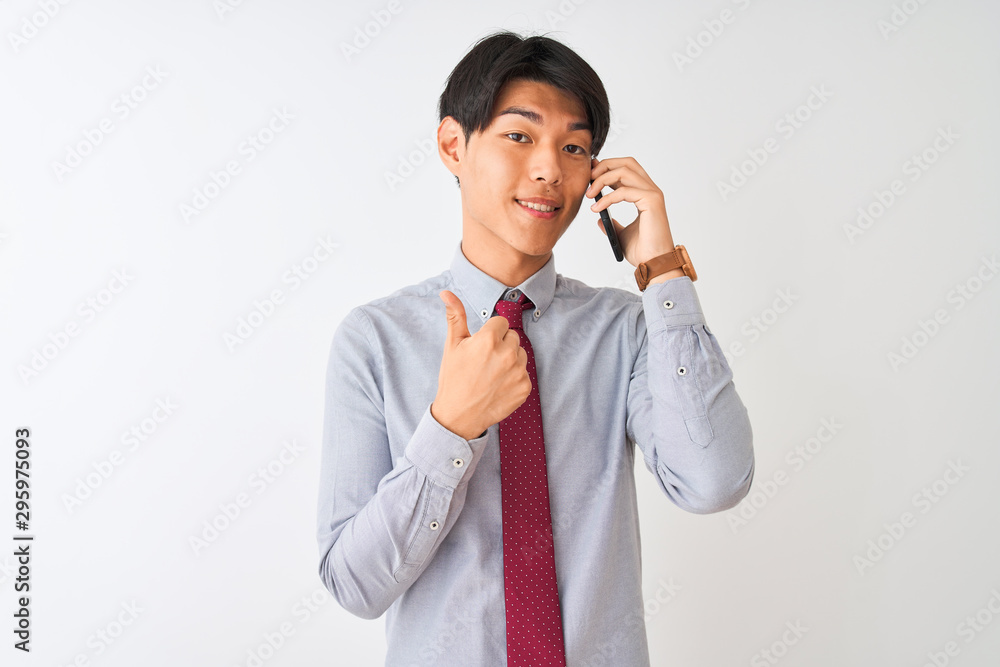 Chinese businessman wearing tie talking on the smartphone over isolated white background happy with big smile doing ok sign, thumb up with fingers, excellent sign Chinese businessman wearing tie talking on the smartphone over isolated white background happy with big smile doing ok sign, thumb up with fingers, excellent sign