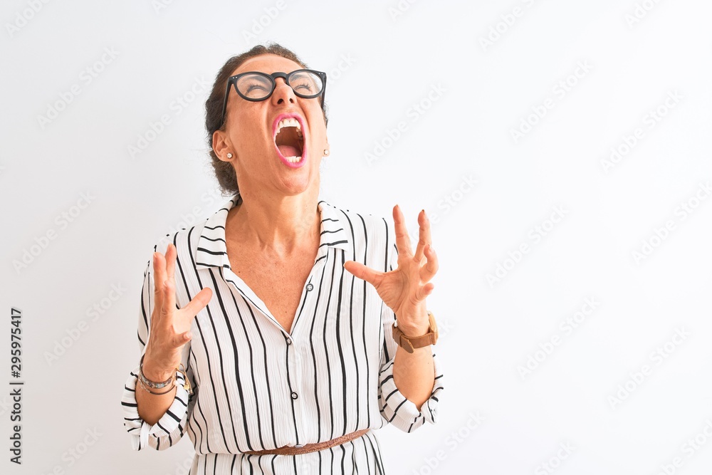 © Krakenimages.com - Middle age businesswoman wearing striped dress and glasses over isolated white background crazy and mad shouting and yelling with aggressive expression and arms raised. Frustration concept.