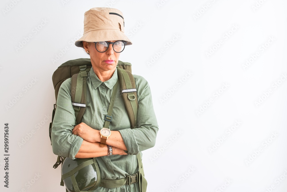 Middle age hiker woman wearing backpack canteen hat glasses over isolated white background skeptic and nervous, disapproving expression on face with crossed arms. Negative person.