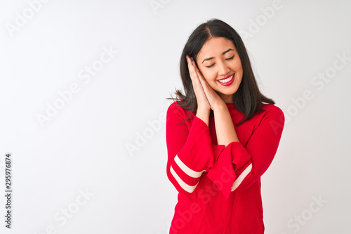 Young beautiful chinese woman wearing red dress standing over isolated white background sleeping tired dreaming and posing with hands together while smiling with closed eyes.