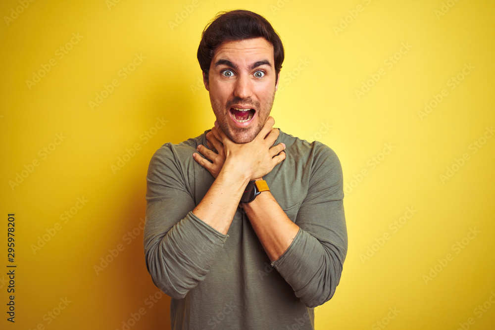 Young handsome man wearing casual t-shirt standing over isolated yellow background shouting and suffocate because painful strangle. Health problem. Asphyxiate and suicide concept. Young handsome man wearing casual t-shirt standing over isolated yellow background shouting and suffocate because painful strangle. Health problem. Asphyxiate and suicide concept.
