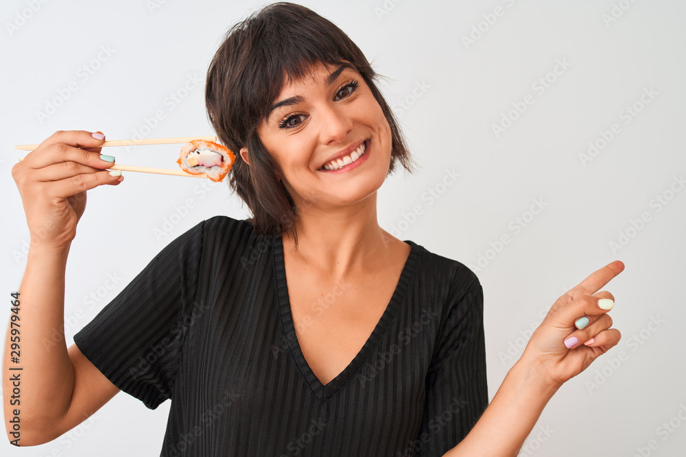 Young beautiful woman eating sushi using chopsticks standing over isolated white background very happy pointing with hand and finger to the side Young beautiful woman eating sushi using chopsticks standing over isolated white background very happy pointing with hand and finger to the side