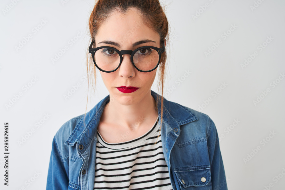 Redhead woman wearing denim shirt and glasses standing over isolated white background with a confident expression on smart face thinking serious