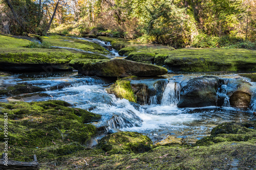 beautiful waterfall inside forest with big rocks covered with green mosses and forest in the background with beautiful autumn colour