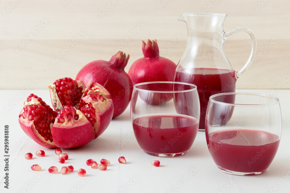 2 glasses of fresh pomegranate juice with few ripe real pomegranates on dark blue background. Partially peeled pomegranate, rouge seeds and peeling knife in foreground. 2 glasses of fresh pomegranate juice with few ripe real pomegranates on dark blue background. Partially peeled pomegranate, rouge seeds and peeling knife in foreground.