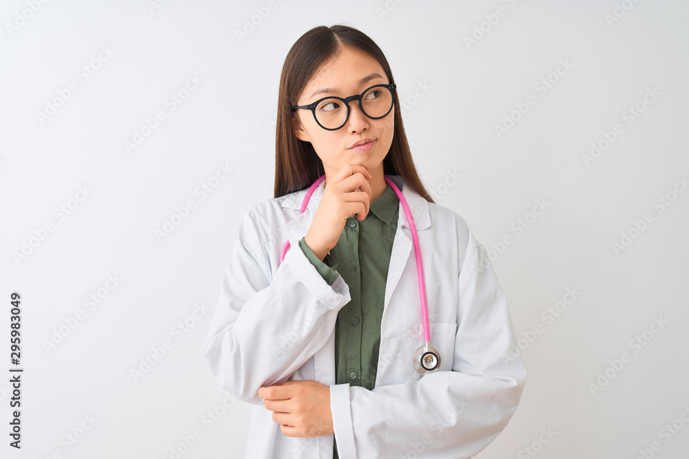 Young chinese dooctor woman wearing glasses stethoscope over isolated white background with hand on chin thinking about question, pensive expression. Smiling with thoughtful face. Doubt concept. Young chinese dooctor woman wearing glasses stethoscope over isolated white background with hand on chin thinking about question, pensive expression. Smiling with thoughtful face. Doubt concept.