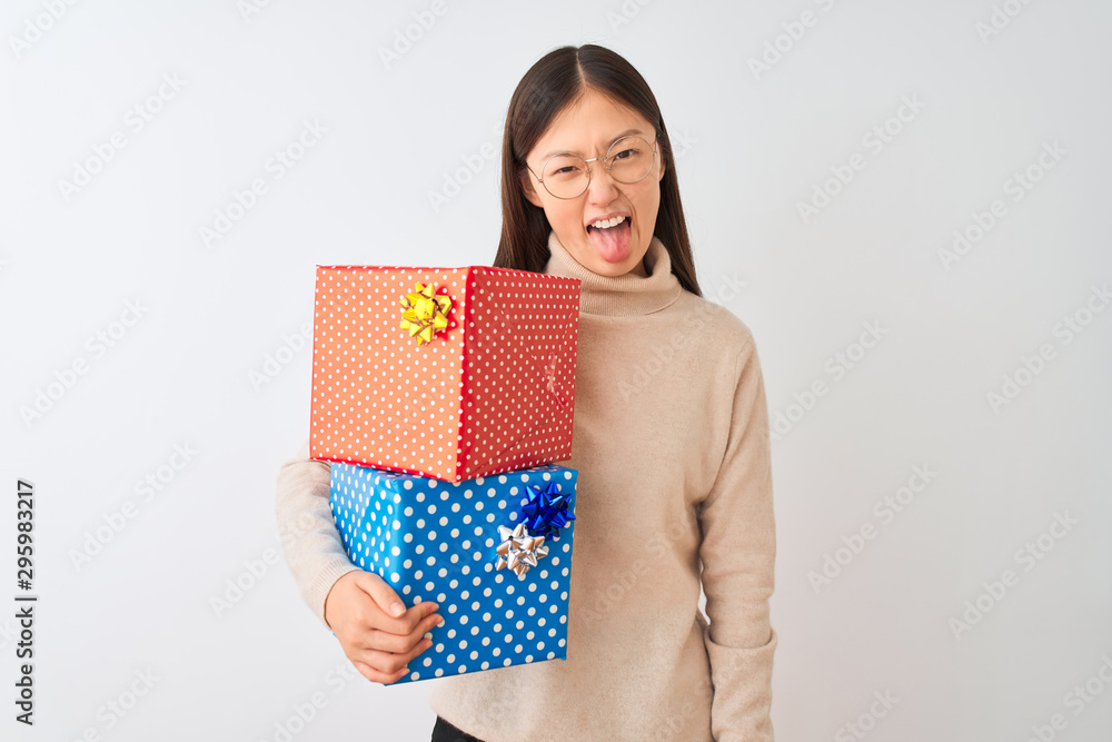 Young chinese woman holding birthday gifts over isolated white background sticking tongue out happy with funny expression. Emotion concept. Young chinese woman holding birthday gifts over isolated white background sticking tongue out happy with funny expression. Emotion concept.