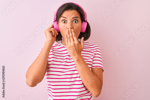 Young beautiful woman listening to music using headphones over isolated pink background cover mouth with hand shocked with shame for mistake, expression of fear, scared in silence, secret concept