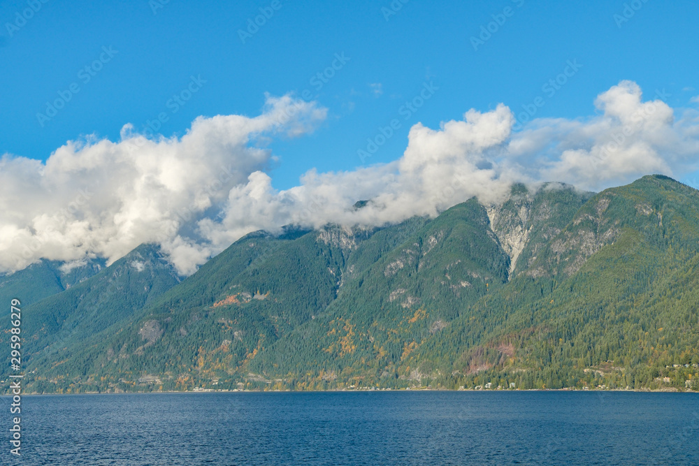 beautiful dense cloud under blue sky over the top of forest covered mountain with a glimpse of autumn colour over the slope on a sunny afternoon by the ocean beautiful dense cloud under blue sky over the top of forest covered mountain with a glimpse of autumn colour over the slope on a sunny afternoon by the ocean