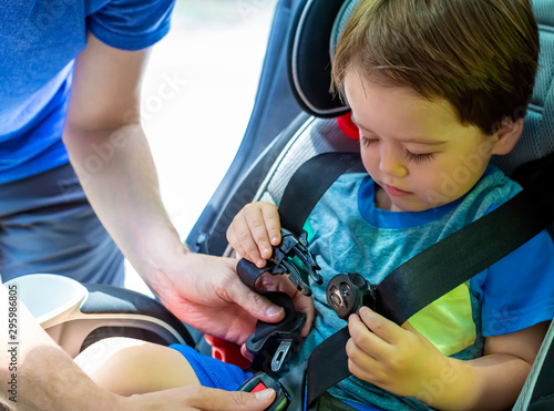 Фотография Toddler boy buckled into his car seat by his father