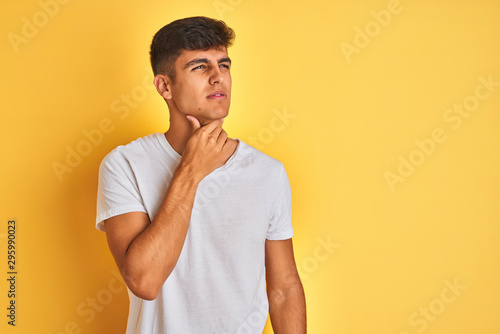 Young indian man wearing white t-shirt standing over isolated yellow background Touching painful neck, sore throat for flu, clod and infection