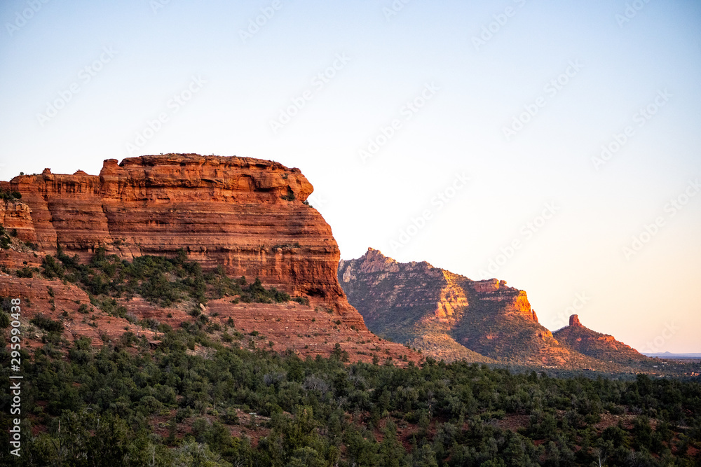 Row of red sandstone formations Capitol Butte glowing at sunset in Sedona, AZ with Coffee Pot Rock in distance