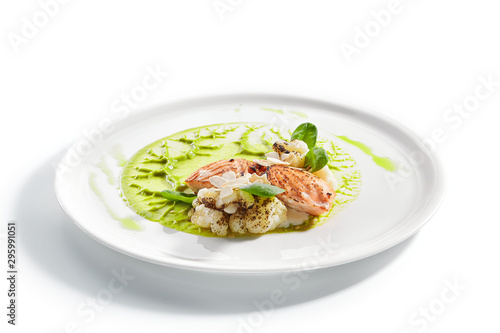 Salmon steak on plate closeup. Red fish piece with green pea puree and cauliflower. Salmon with creamy sauce and vegetables isolated on white background. Restaurant tasty dish, cooked healthy meal