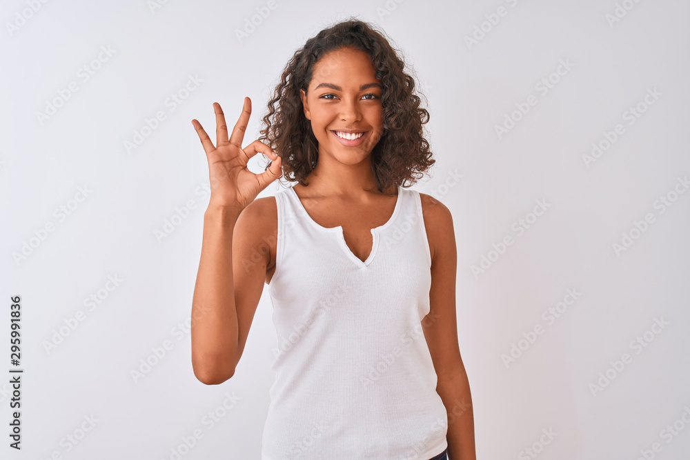 Young brazilian woman wearing casual t-shirt standing over isolated white background smiling positive doing ok sign with hand and fingers. Successful expression. Young brazilian woman wearing casual t-shirt standing over isolated white background smiling positive doing ok sign with hand and fingers. Successful expression.