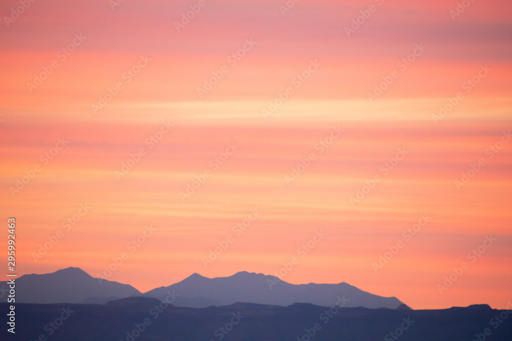 Dramatic sunset over blue mountain silhouettes in orange and pink colors. Majestic background texture with copy space.