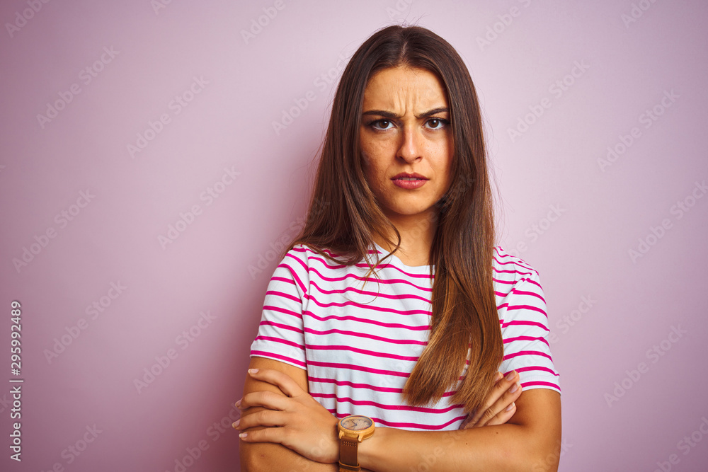 Young beautiful woman wearing striped t-shirt standing over isolated pink background skeptic and nervous, disapproving expression on face with crossed arms. Negative person. Young beautiful woman wearing striped t-shirt standing over isolated pink background skeptic and nervous, disapproving expression on face with crossed arms. Negative person.