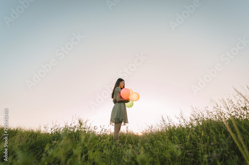 Tone film of lonely asian woman holding colorful balloons on green field with sunset time