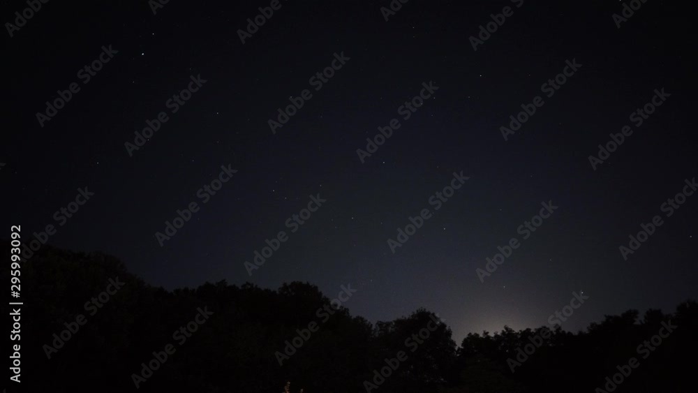 Motion Time Lapse of night sky with stars and the moon hiding in the silhouette of a forest Motion Time Lapse of night sky with stars and the moon hiding in the silhouette of a forest