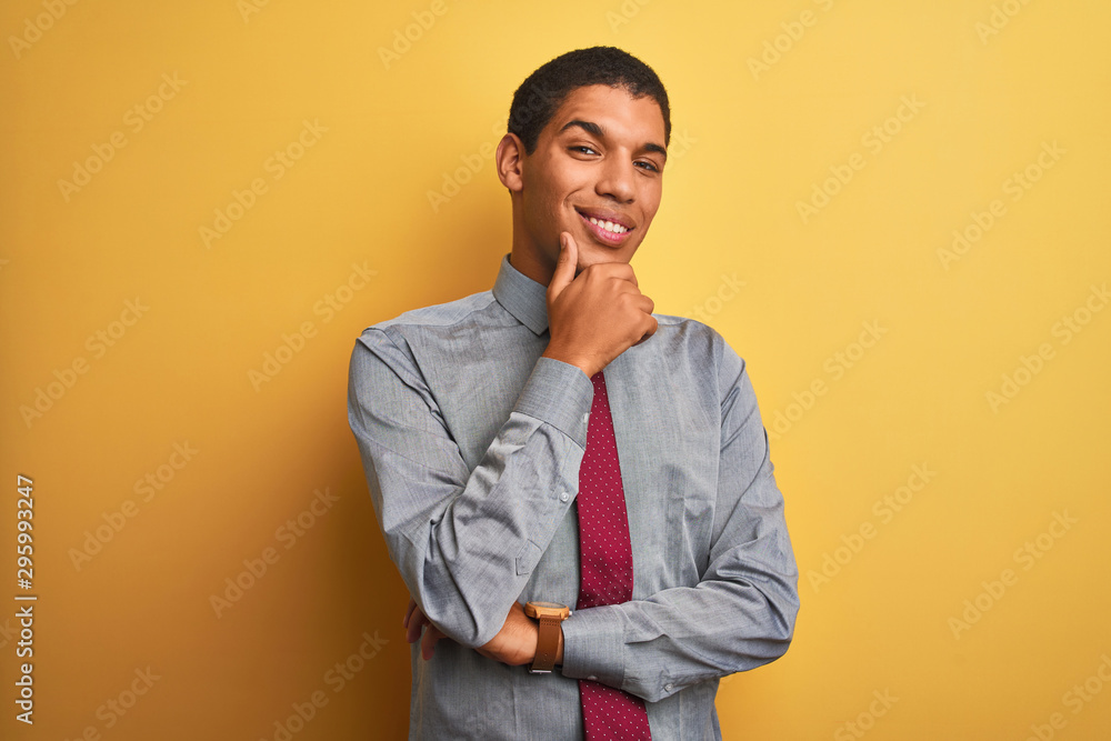 Young handsome arab businessman wearing shirt and tie over isolated yellow background looking confident at the camera smiling with crossed arms and hand raised on chin. Thinking positive. Young handsome arab businessman wearing shirt and tie over isolated yellow background looking confident at the camera smiling with crossed arms and hand raised on chin. Thinking positive.