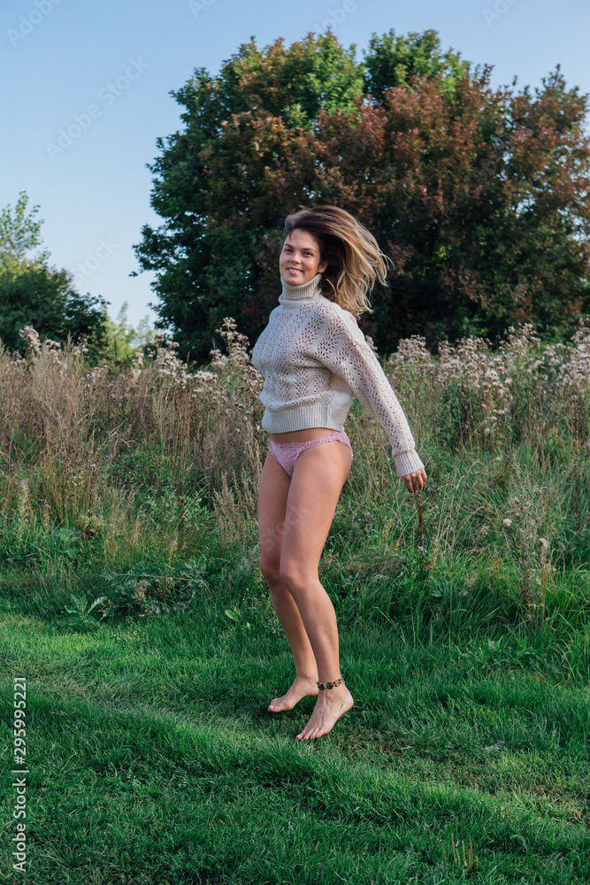 Happy young beautiful woman jumping with bare foot in a green field