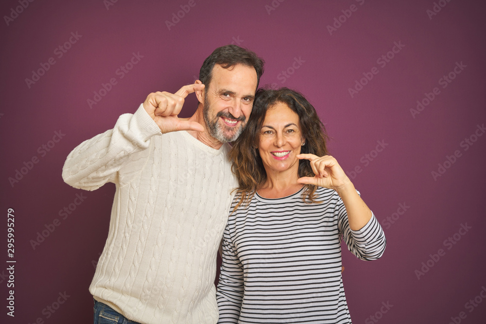 Beautiful middle age couple wearing winter sweater over isolated purple background smiling and confident gesturing with hand doing small size sign with fingers looking and the camera. Measure concept. Beautiful middle age couple wearing winter sweater over isolated purple background smiling and confident gesturing with hand doing small size sign with fingers looking and the camera. Measure concept.