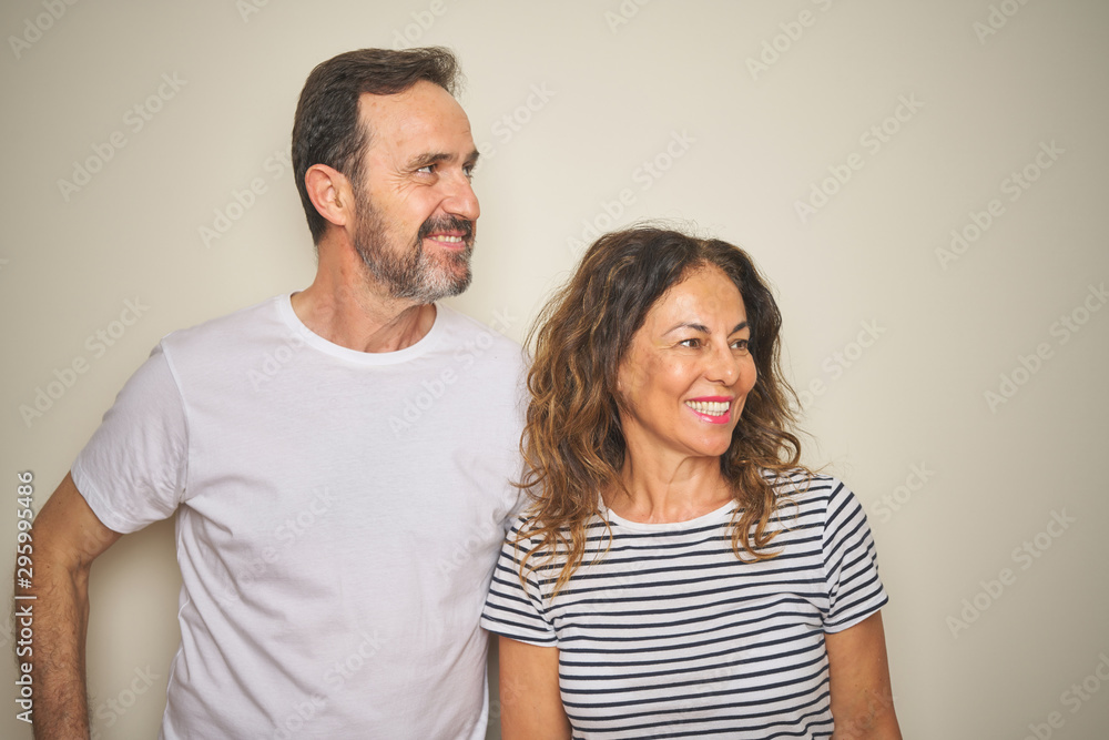 Beautiful middle age couple together standing over isolated white background looking away to side with smile on face, natural expression. Laughing confident. Beautiful middle age couple together standing over isolated white background looking away to side with smile on face, natural expression. Laughing confident.