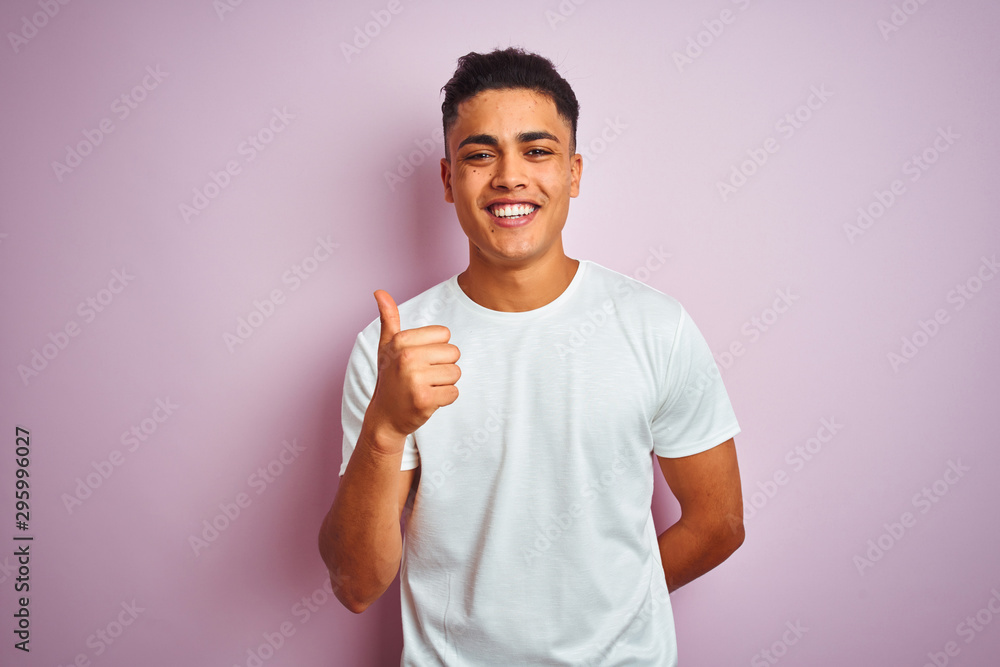 Young brazilian man wearing t-shirt standing over isolated pink background doing happy thumbs up gesture with hand. Approving expression looking at the camera with showing success. Young brazilian man wearing t-shirt standing over isolated pink background doing happy thumbs up gesture with hand. Approving expression looking at the camera with showing success.