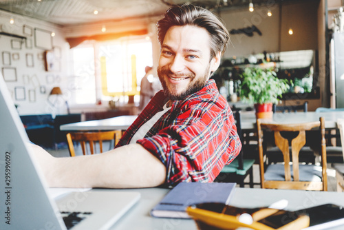 Portrait of smiling stubbled man working with laptop in big bright office space