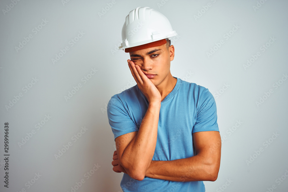 Young brazilian engineer man wearing security helmet standing over isolated white background thinking looking tired and bored with depression problems with crossed arms. Young brazilian engineer man wearing security helmet standing over isolated white background thinking looking tired and bored with depression problems with crossed arms.