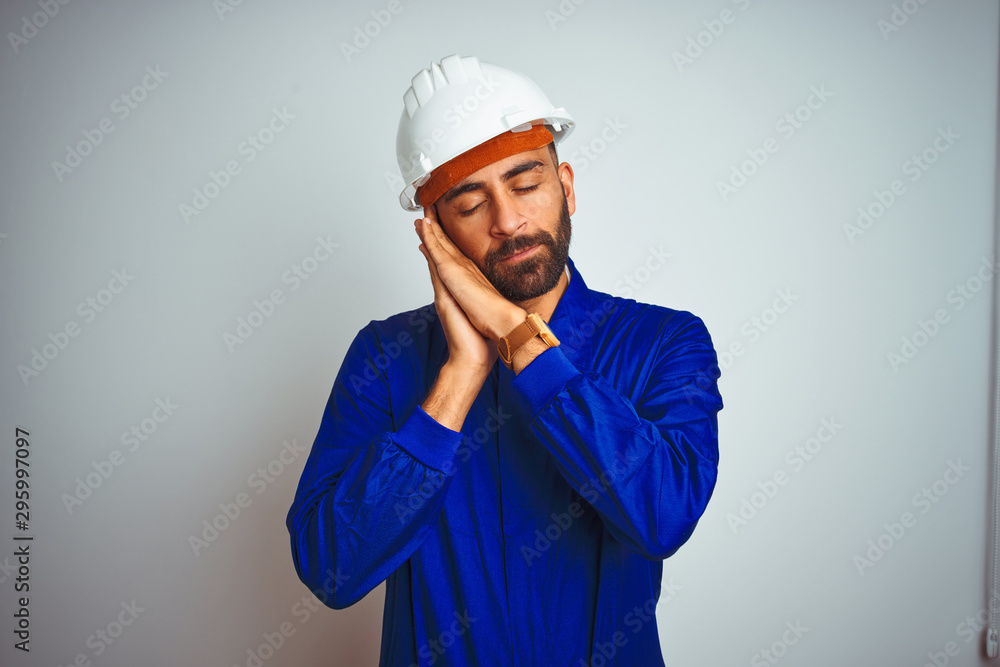 Handsome indian worker man wearing uniform and helmet over isolated white background sleeping tired dreaming and posing with hands together while smiling with closed eyes. Handsome indian worker man wearing uniform and helmet over isolated white background sleeping tired dreaming and posing with hands together while smiling with closed eyes.