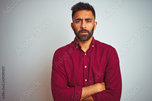Fotografie, Obraz Young indian man wearing red elegant shirt standing over isolated grey background skeptic and nervous, disapproving expression on face with crossed arms