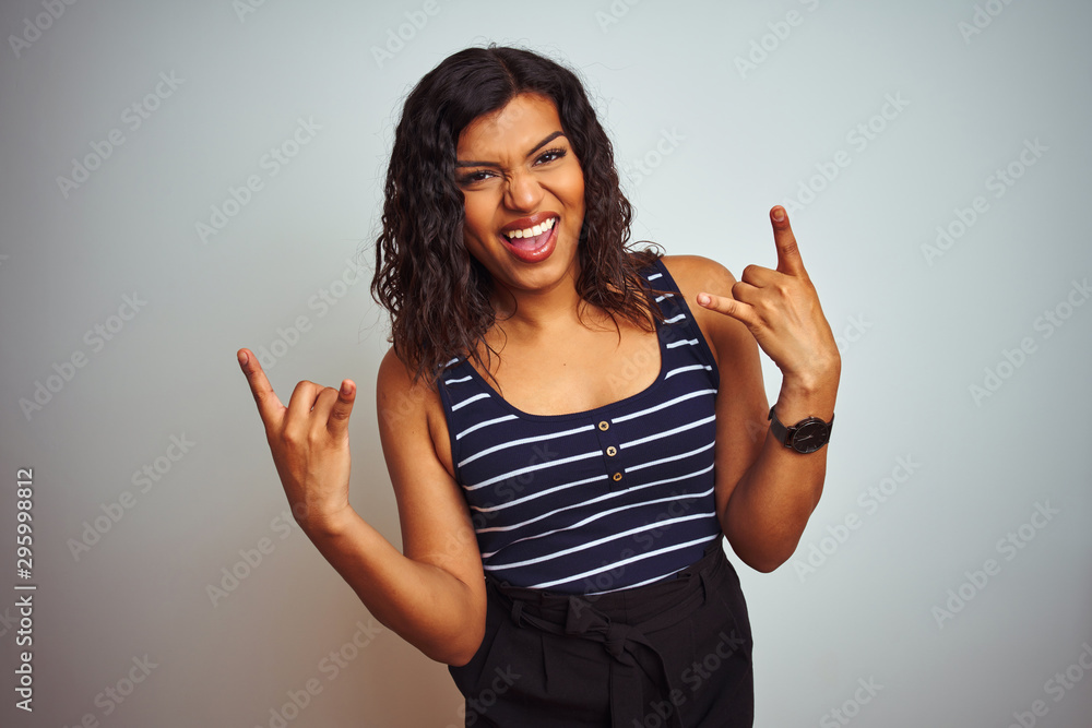 Transsexual transgender woman wearing striped t-shirt over isolated white background shouting with crazy expression doing rock symbol with hands up. Music star. Heavy music concept. Transsexual transgender woman wearing striped t-shirt over isolated white background shouting with crazy expression doing rock symbol with hands up. Music star. Heavy music concept.