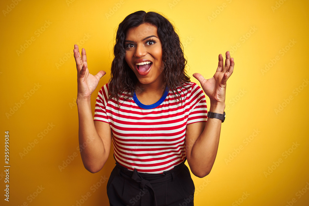 Transsexual transgender woman wearing stiped t-shirt over isolated yellow background celebrating crazy and amazed for success with arms raised and open eyes screaming excited. Winner concept Transsexual transgender woman wearing stiped t-shirt over isolated yellow background celebrating crazy and amazed for success with arms raised and open eyes screaming excited. Winner concept