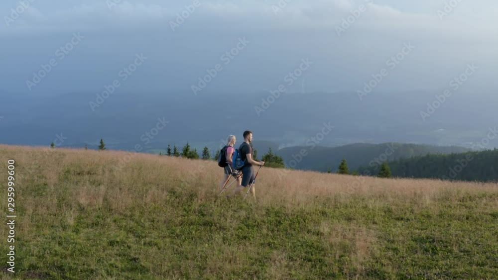 An adventurous backpacker couple hiking/trekking down the beautiful green mountains after accomplishing the peak with mesmerizing landscape in background. Aerial drone. An adventurous backpacker couple hiking/trekking down the beautiful green mountains after accomplishing the peak with mesmerizing landscape in background. Aerial drone.