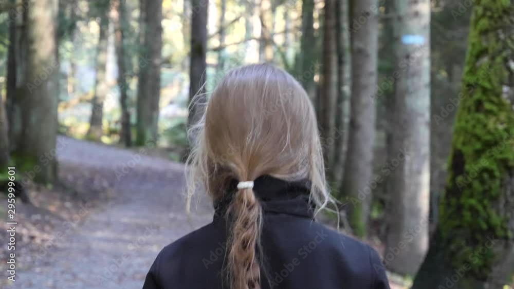 A young girl with long braided hair walks along a path alone - follow from behind view A young girl with long braided hair walks along a path alone - follow from behind view