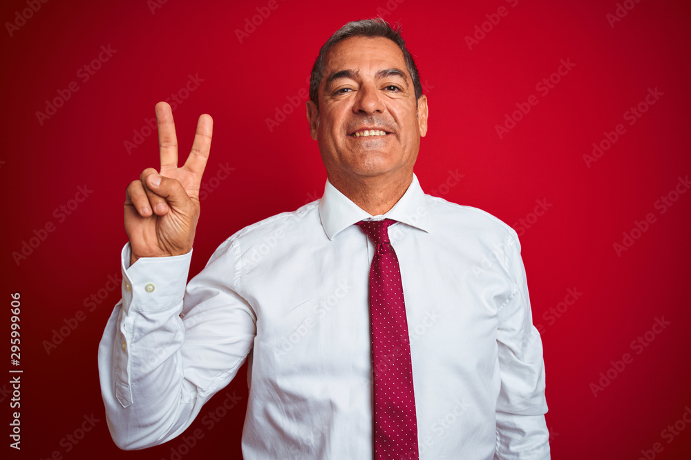 Handsome middle age businessman standing over isolated red background showing and pointing up with fingers number two while smiling confident and happy. Handsome middle age businessman standing over isolated red background showing and pointing up with fingers number two while smiling confident and happy.