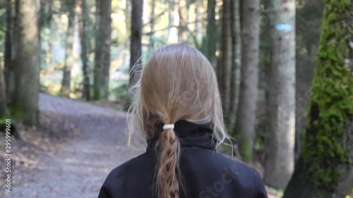 A young girl with long braided hair walks along a path alone - follow from behind view photo