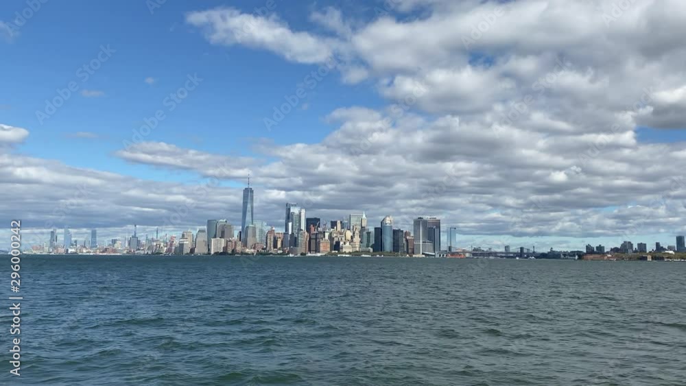 New York Manhattan skyline and waterfront filmed from cruise boat passing by. Wide establishing shot with blue sky and clouds. New York Manhattan skyline and waterfront filmed from cruise boat passing by. Wide establishing shot with blue sky and clouds.