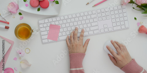 Overhead shot of young girl typing on keyboard in sweet pink feminine workspace with make up